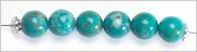 six turquoise round beads and two silver-plated bead caps, strung onto beading wire.
